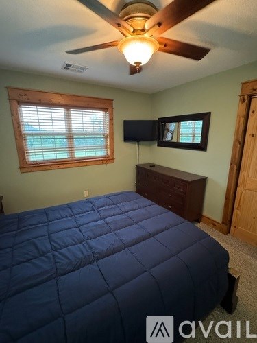 A bedroom with a bed, ceiling fan, and a window.