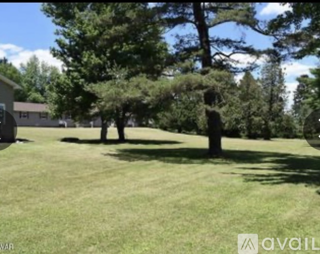 A grassy field with trees and a house in the background.