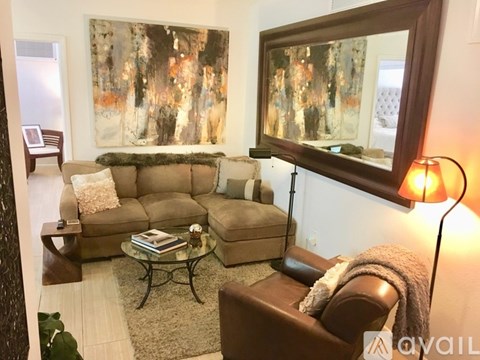 A living room with a brown couch, a glass coffee table, and a large painting on the wall.