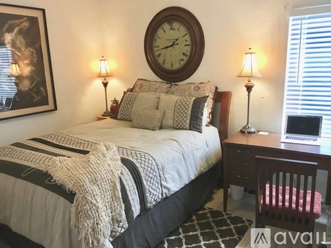 A bedroom with a bed, a desk with a laptop, and a clock on the wall.