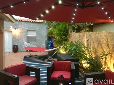 A patio with red chairs and a table under a red umbrella.