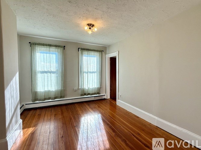 A room with wooden floors and two windows with curtains.