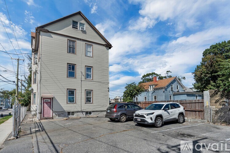 A grey building with a red door and a parking lot in front.