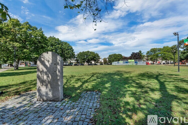 A large stone monument sits in the middle of a park with a cobblestone pathway leading up to it.