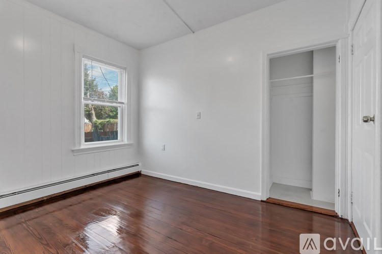A room with wooden floors and white walls, with a window and a door visible.