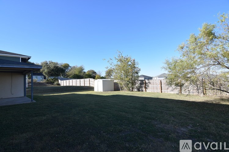 A sunny day at a grassy field with a building and trees in the background.