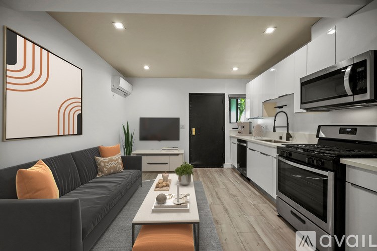 A modern kitchen with a black sofa and orange pillows.
