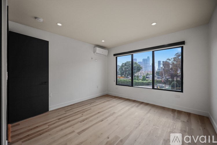 A spacious room with wooden flooring and a large window overlooking a cityscape.