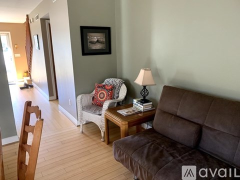 A living room with a brown couch, a chair, a small table with a lamp and a picture frame on the wall.