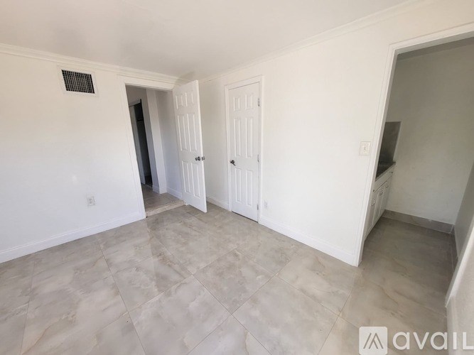 A room with white walls and a tiled floor with a doorway leading to another room.