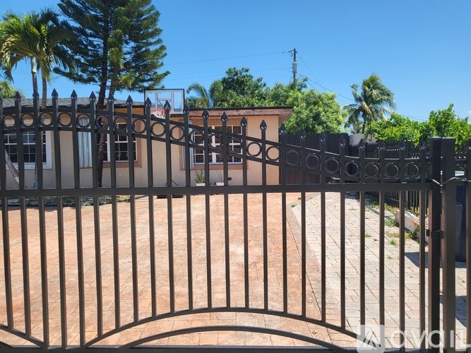 A black metal gate with a curved top leads to a building with a brown roof.