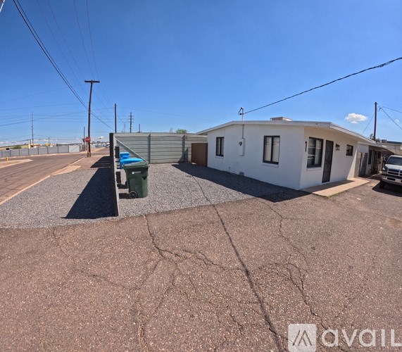 A small white house with a grey roof is situated in a parking lot.