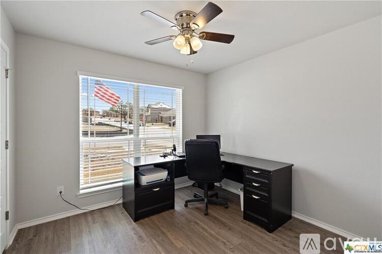 A room with a desk, chair, and a ceiling fan.