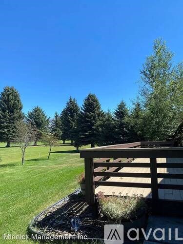 A wooden deck overlooks a grassy field with trees in the distance.