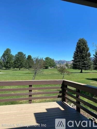A wooden deck overlooks a grassy field with trees and distant mountains.