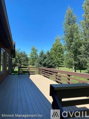 A wooden deck with a bench and trees in the background.