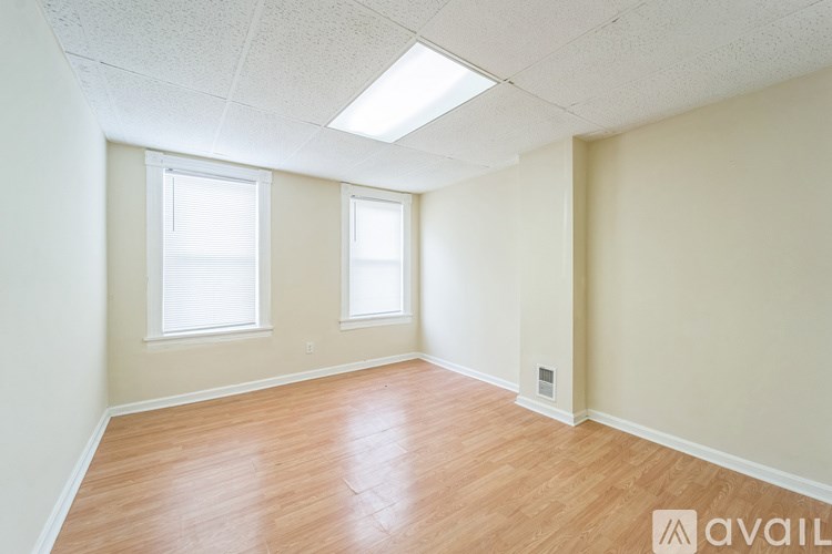 A room with wooden flooring and two windows.