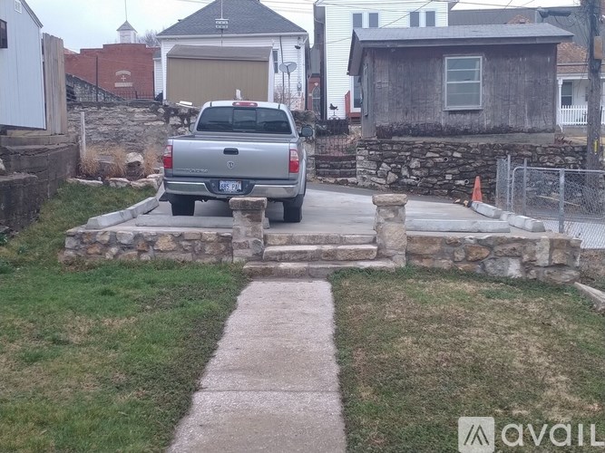 A silver truck is parked in front of a stone wall.