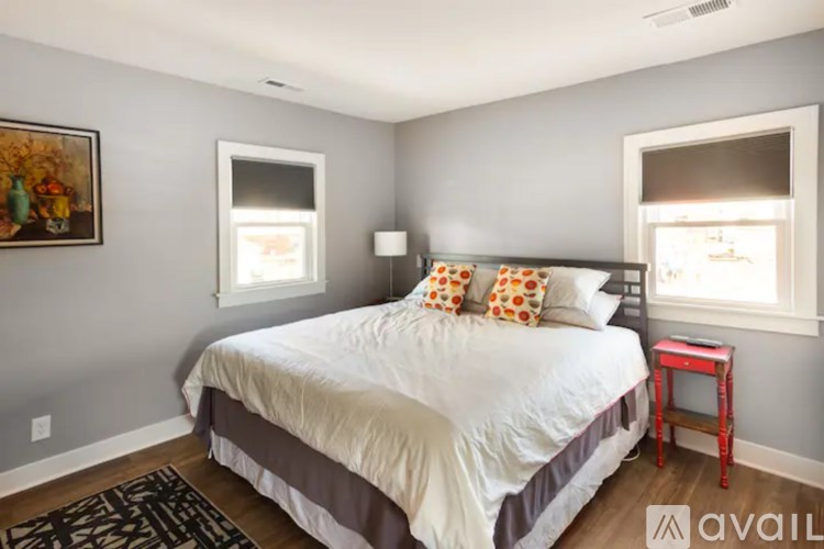 A bedroom with a bed, a small table, and two windows.