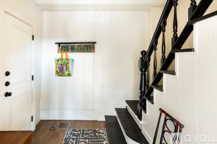 A hallway with a wooden floor, a staircase with black railings, and a door with black knobs.
