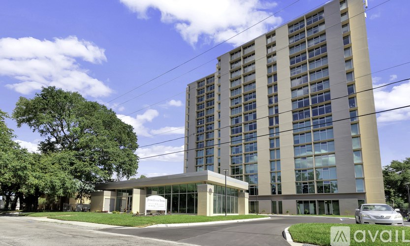 A tall building with a glass facade is surrounded by trees and has a car parked in front.