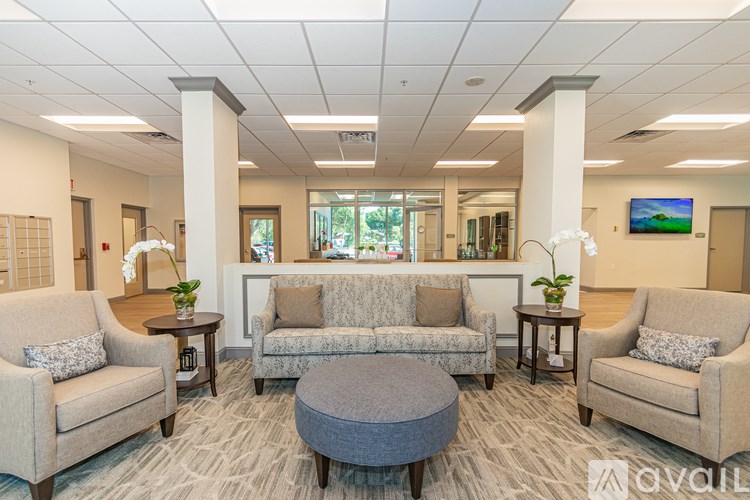 A waiting room with beige chairs and a grey ottoman.