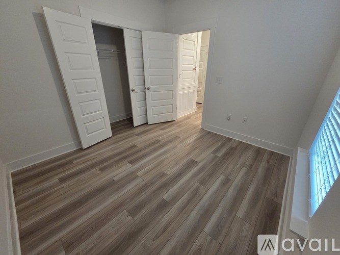A room with wooden flooring and white walls, featuring a set of white doors.