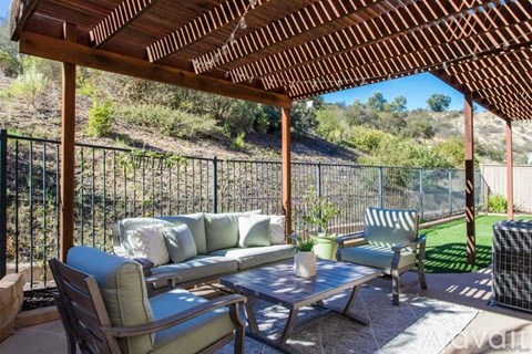 A patio with a couch, chairs, and a table under a wooden pergola.