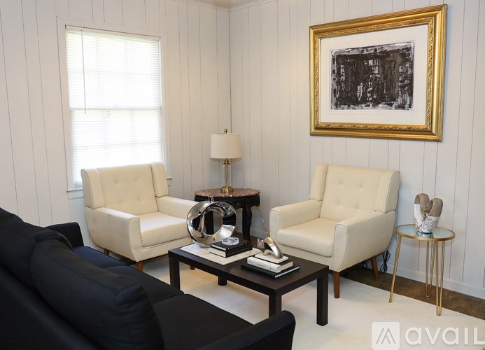 A living room with a black couch, two white chairs, and a coffee table.