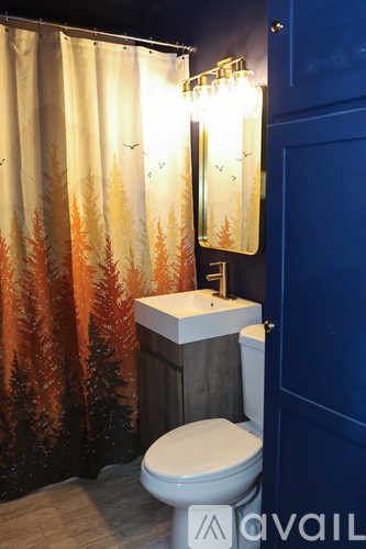 A bathroom with a white toilet and a shower curtain with trees on it.