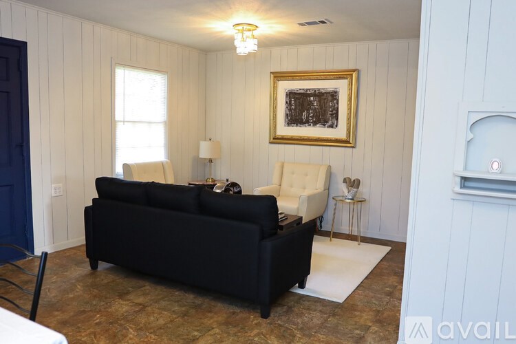 A black couch sits in a room with a wooden floor and white walls.