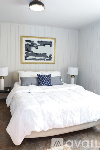 A bedroom with a white bed and a framed artwork on the wall.
