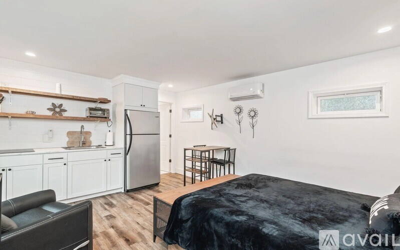 A bedroom with a black bed and a kitchen area with white cabinets and a fridge.