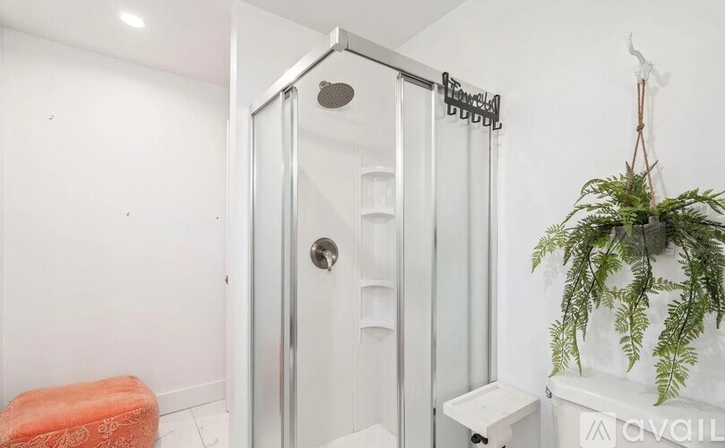 A white bathroom with a glass shower door and a plant on the window sill.