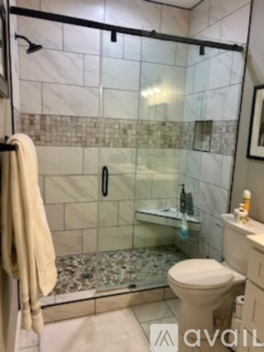 A bathroom with a toilet, a glass shower stall, and a towel hanging on a rack.