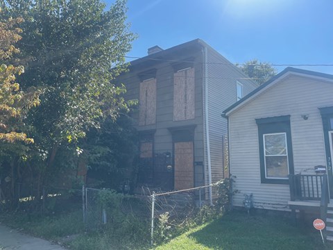 A house with boarded up windows sits next to a tree.