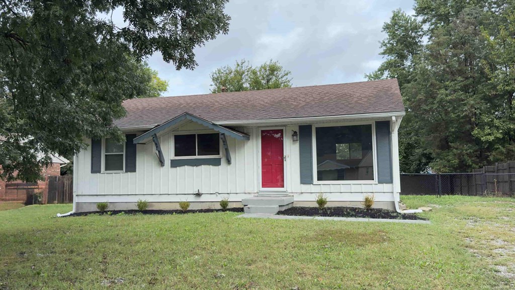 A small white house with a red door is surrounded by a grassy area.
