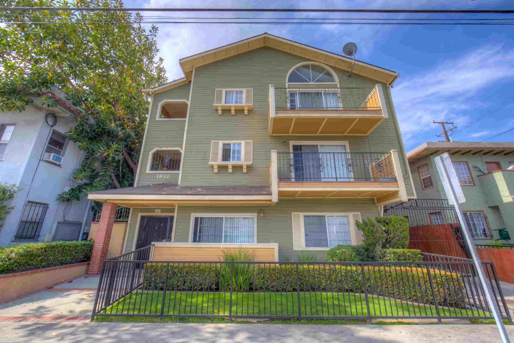 A two-story apartment building with a green exterior and a black fence in front.