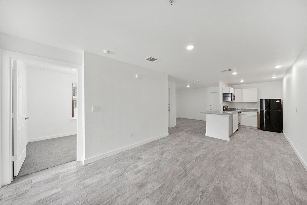 A spacious, empty room with a kitchenette in the background.