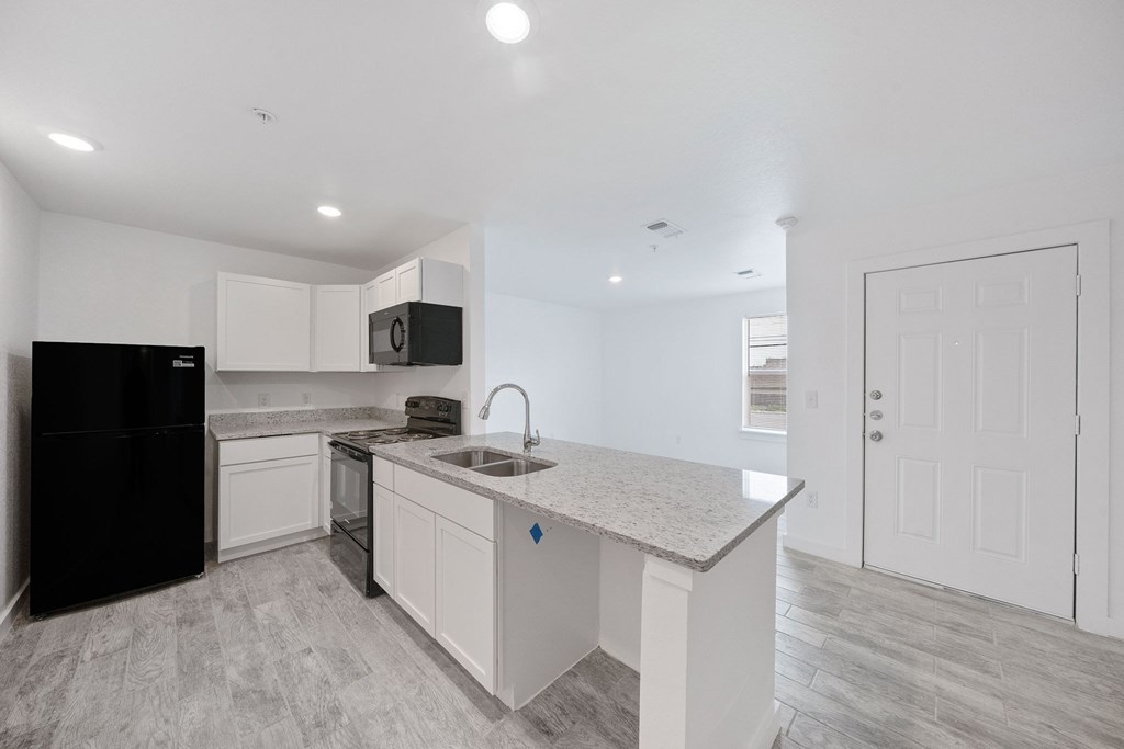A kitchen with a black fridge, white cabinets, and a granite countertop.