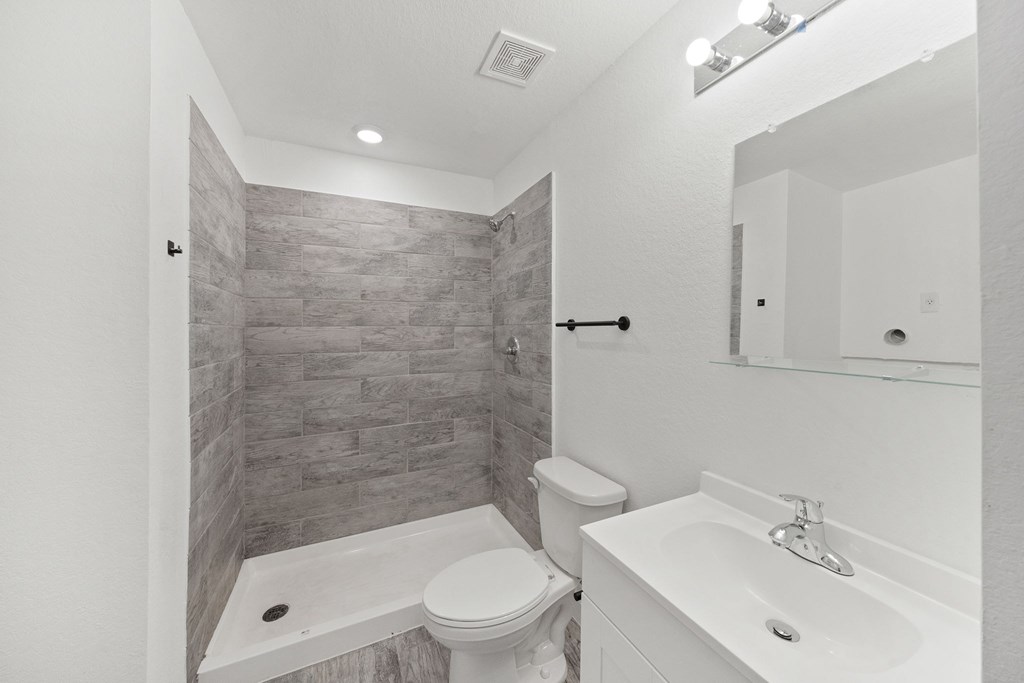 A bathroom with a toilet, sink, and a tiled shower.