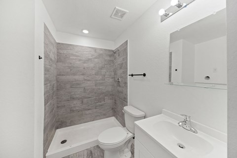 A bathroom with a toilet, sink, and a tiled shower.