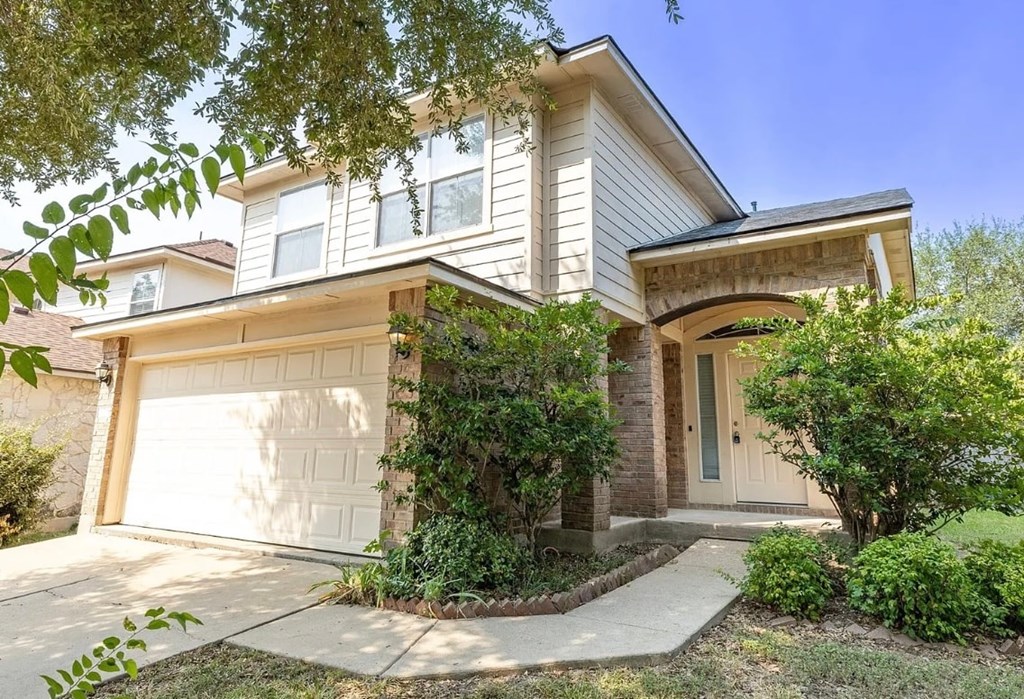 A house with a white garage door is surrounded by greenery.
