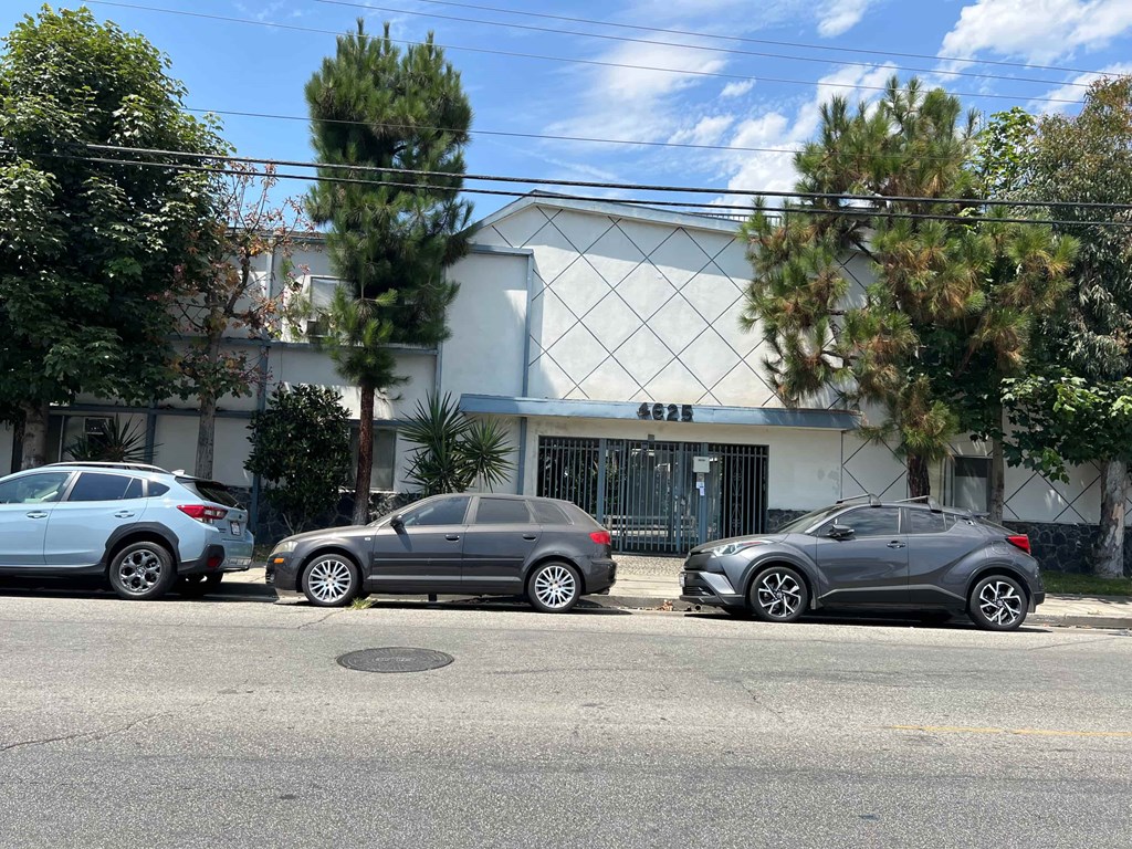 Three cars parked in front of a white building with a black gate.