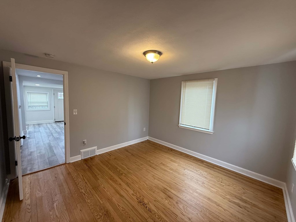 A room with wooden flooring and a window with blinds.