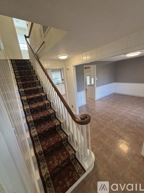 A staircase with a red carpeted runner and white balusters leads to a second floor.