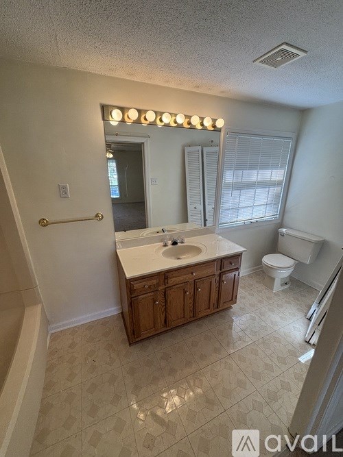 A bathroom with a sink, toilet, and a mirror with lights above it.