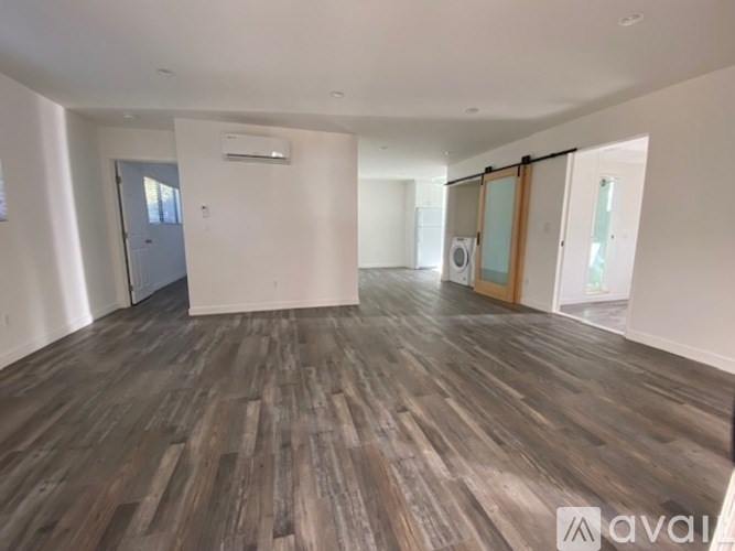 A spacious room with wooden flooring and a sliding glass door.