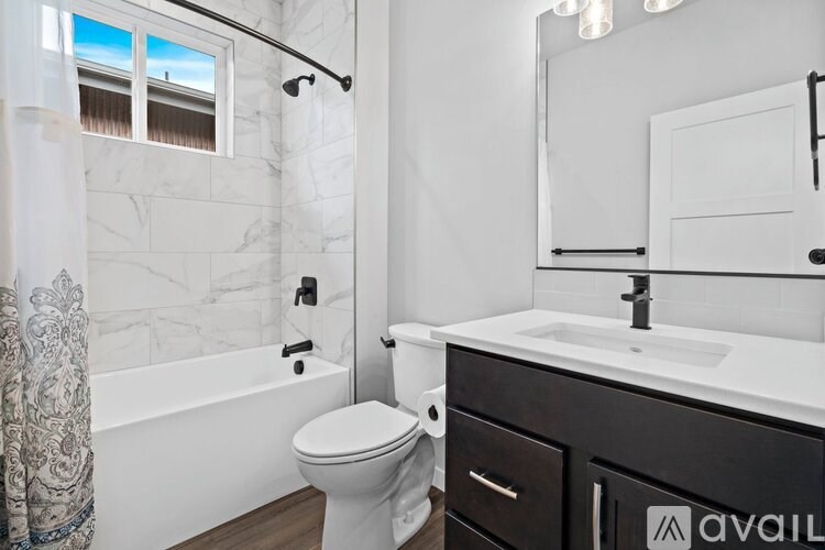 A bathroom with a white toilet, a bathtub with a shower curtain, a sink, and a mirror.