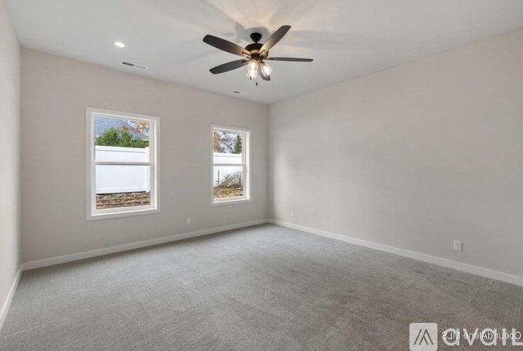 A spacious room with a ceiling fan and two windows.
